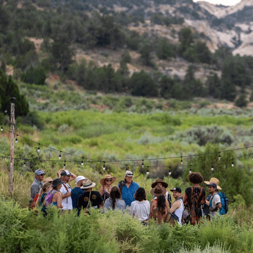 A group of people standing in a circle outside surrounded by mountains and trees.