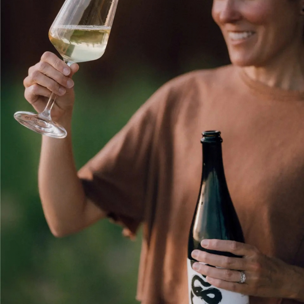 Woman holfing a glass of white wine in one hand an wine bottle in the other.